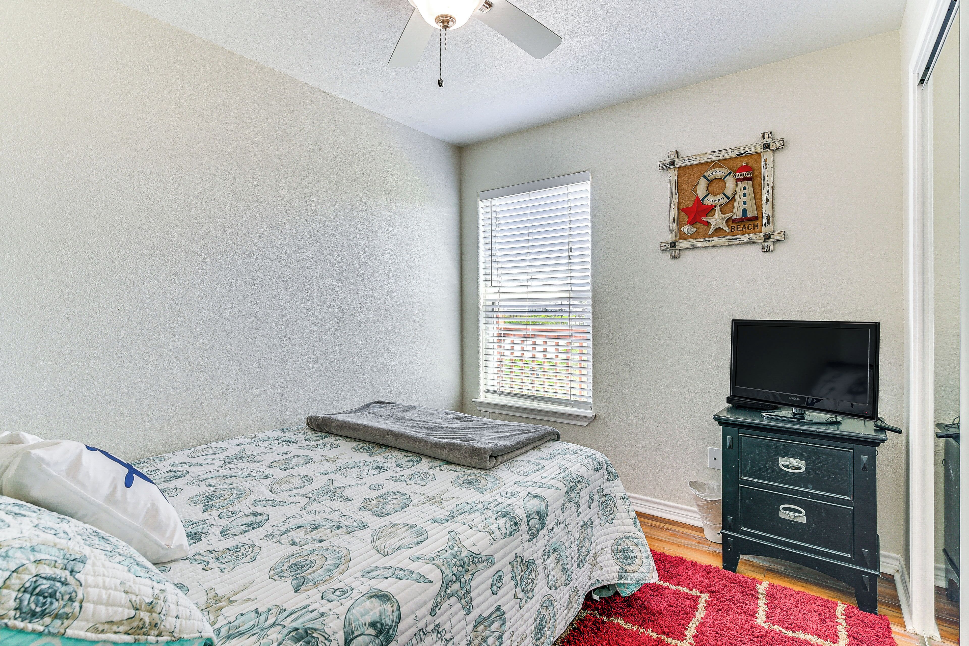 A bedroom with a bed, a TV stand, and a window with blinds.