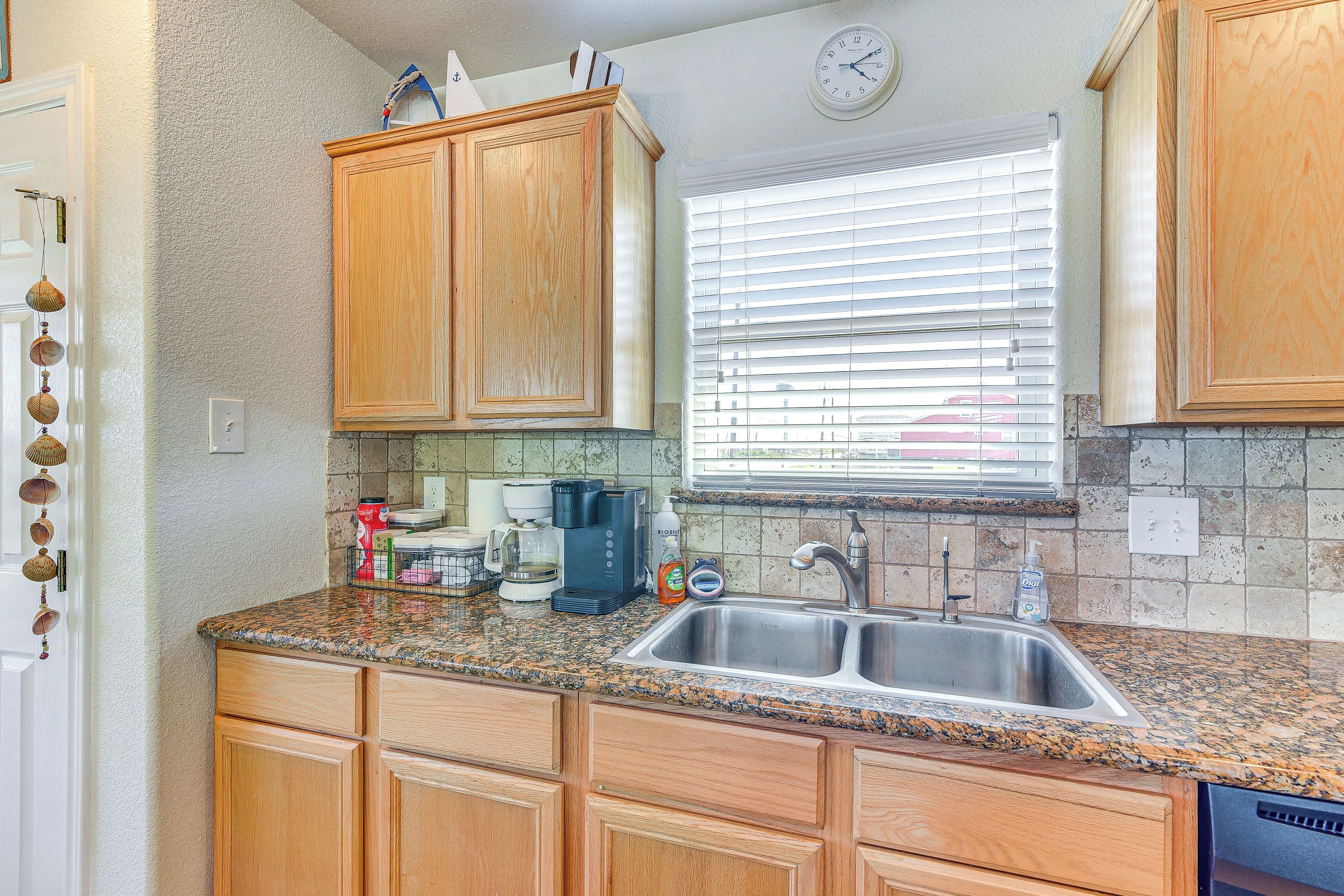A kitchen with wooden cabinets, granite countertops, a stainless steel sink, and a window with blinds.