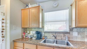 A kitchen with wooden cabinets, granite countertops, a stainless steel sink, and a window with blinds. - Steps to Surfside Beach With Easy Ramp Access! (Freeport)