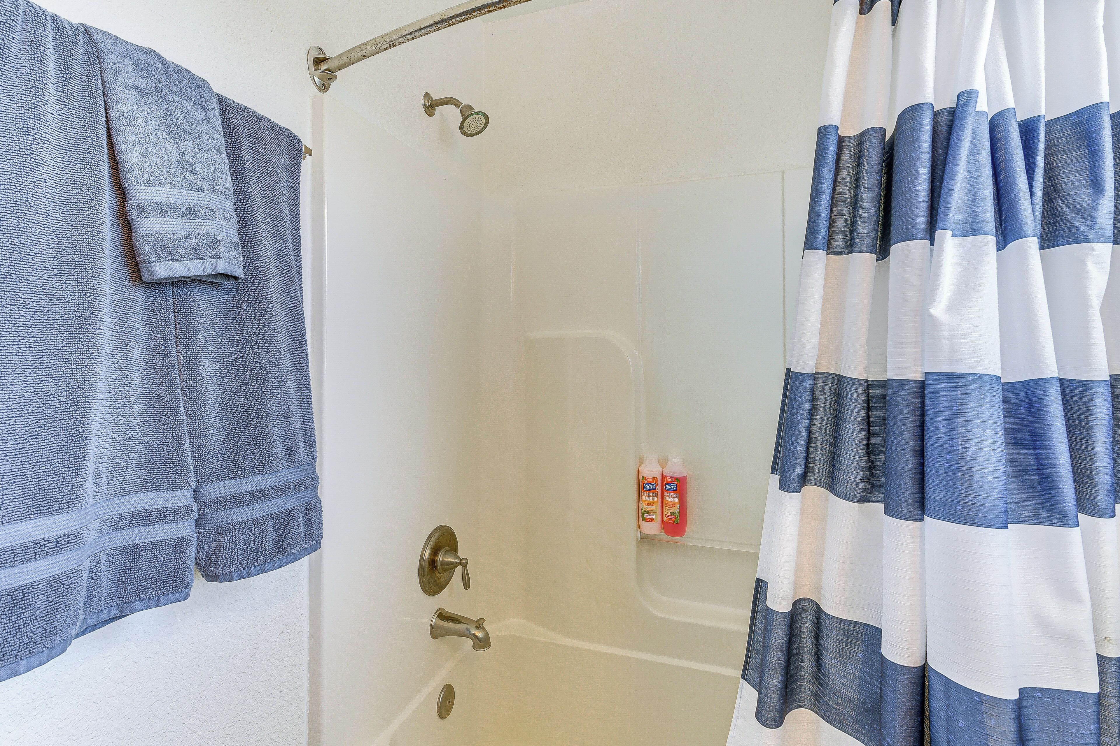 A bathroom with a shower curtain, a towel rack, and a bottle of shampoo.