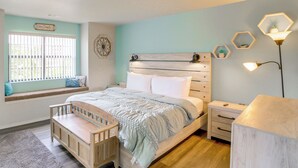 Ein Schlafzimmer mit Bett, einer Bank, einem Nachttisch, einer Lampe und einem Fenster mit Jalousien.
