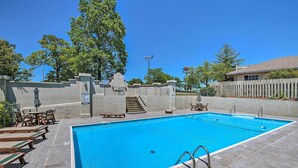 Ein rechteckiger Swimmingpool mit klarem, blauem Wasser, umgeben von einer Betonplattform, Holzliegen und einer kleinen Treppe zu einem überdachten Bereich.