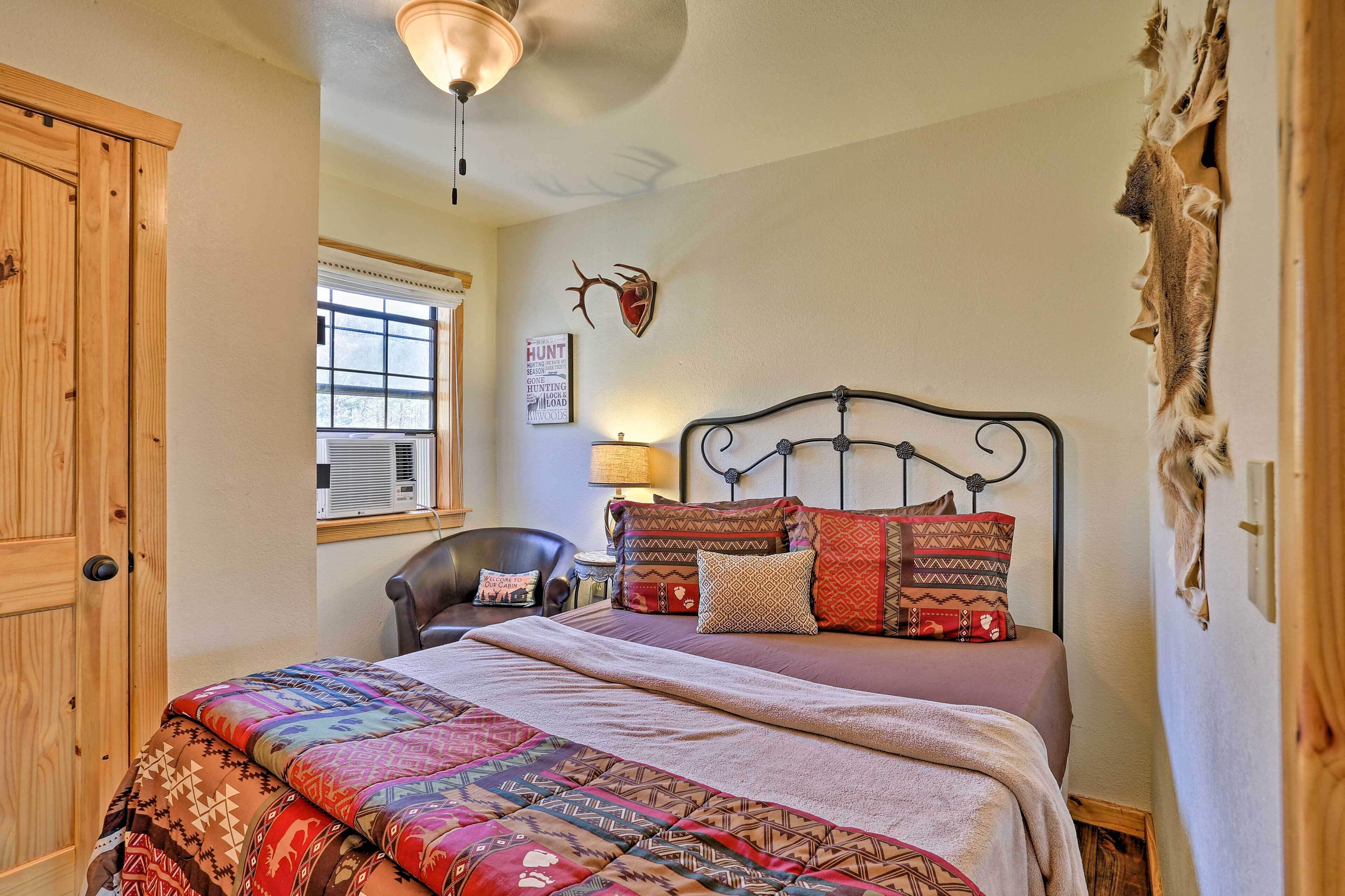 A bedroom with a large bed, a wooden wardrobe, a window with blinds, a wall-mounted deer head decoration, and a wall-mounted lamp.