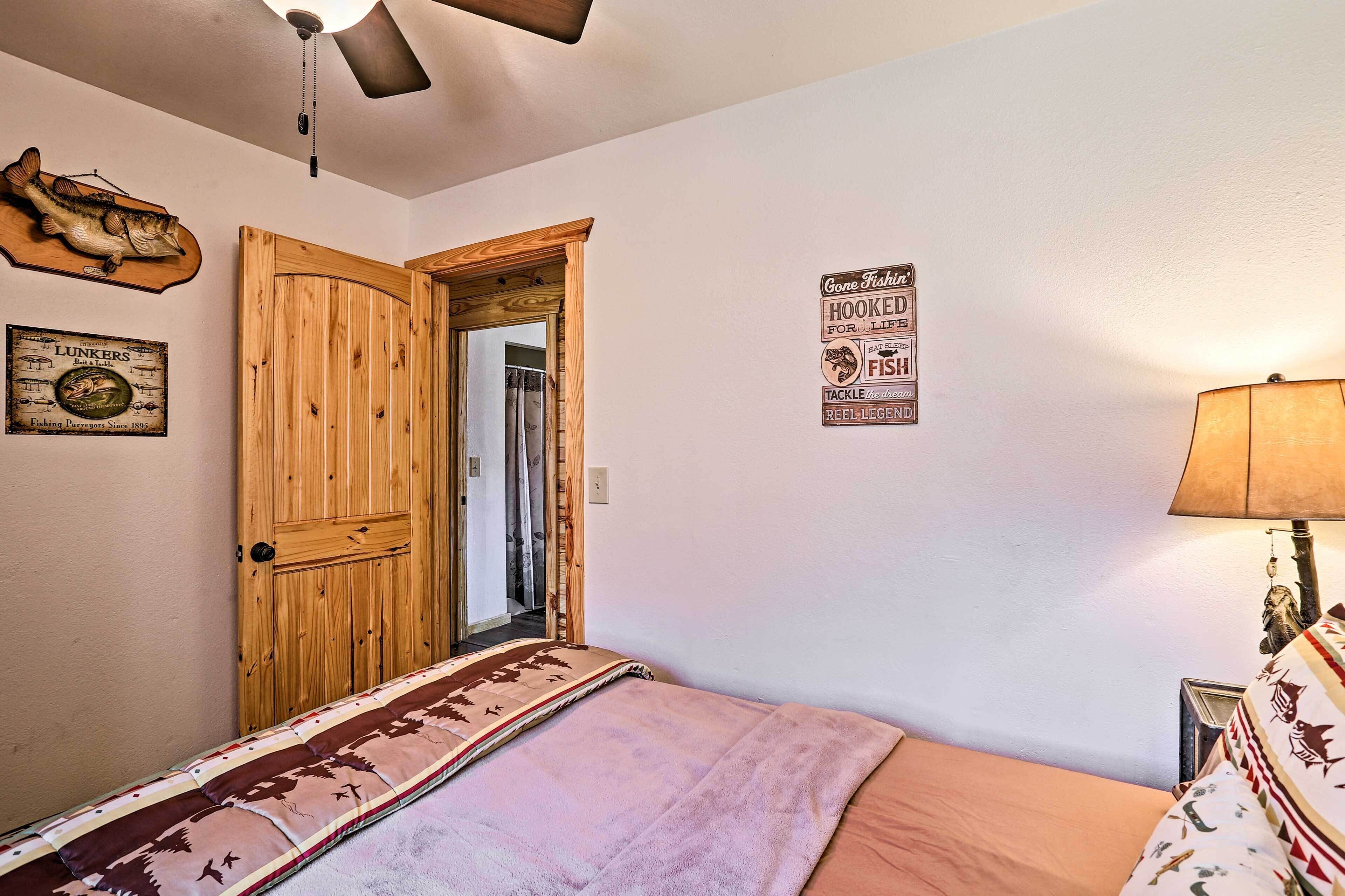 A bedroom with a wooden door, a bed with a patterned blanket, a wall-mounted lamp, and a ceiling fan.