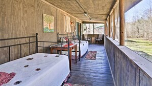 A covered porch with two beds, a table, and a chair. - Serene Cabins w/ Decks & 8 Acres on Kiamichi River (Hodgen)