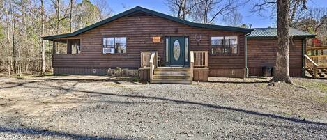 A rustic cabin with a green door, wooden porch, and a gravel driveway.