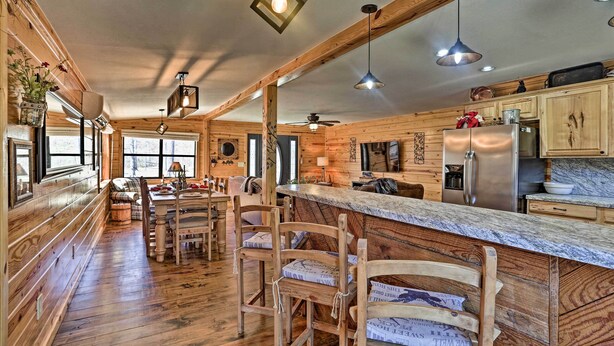 A rustic kitchen with wooden walls, a marble countertop, and a central island with bar stools. - Serene Cabins w/ Decks & 8 Acres on Kiamichi River (Hodgen)