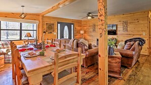A wooden interior with a dining table, chairs, a sofa, and a television. - Serene Cabins w/ Decks & 8 Acres on Kiamichi River (Hodgen)