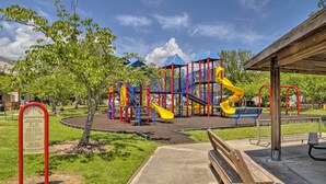 A playground with slides and climbing structures, surrounded by trees and a wooden bench.