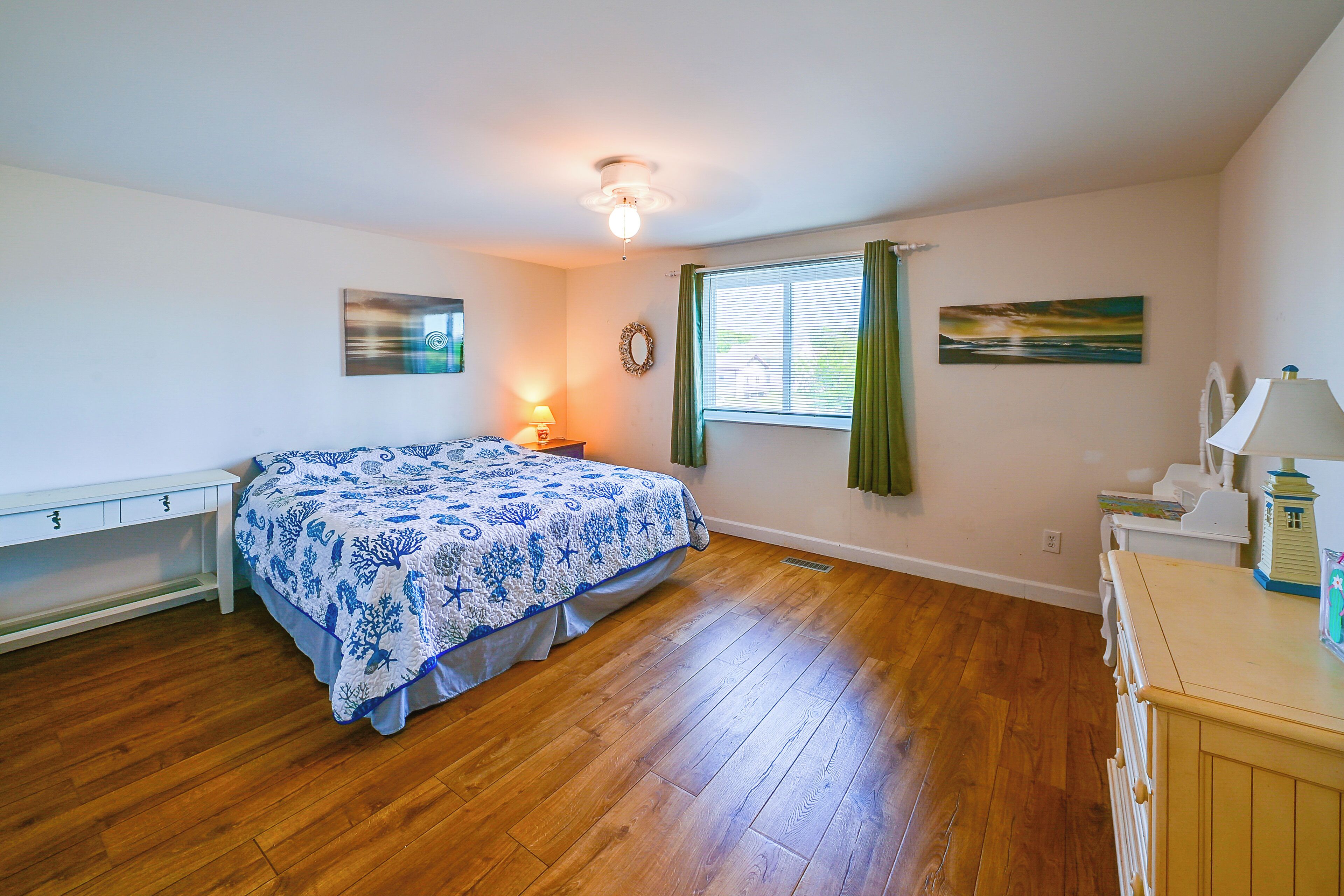 A bedroom with a bed, a nightstand, a dresser, a window with curtains, and a ceiling fan.