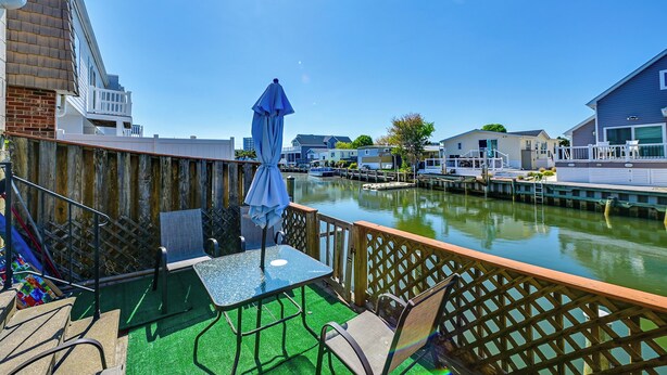 A waterfront patio with a table and chairs, a wooden deck, and a view of the water and buildings.