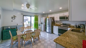 A modern kitchen with white cabinets, stainless steel appliances, a dining area with wicker chairs, and a green curtain.