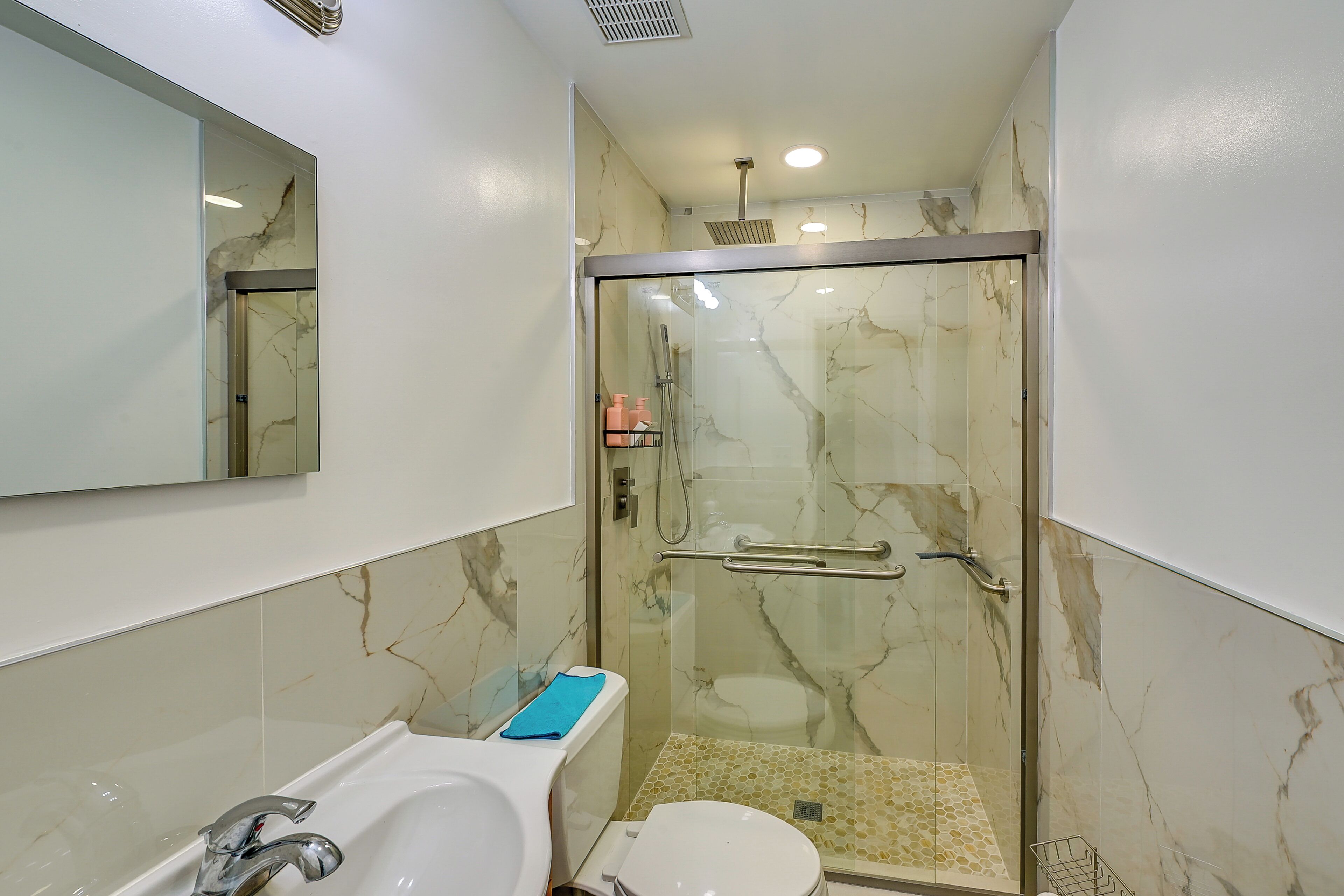 A bathroom with a glass-enclosed shower, a white sink, and a toilet.