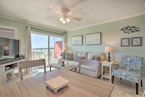 A spacious living area with a sofa, coffee table, and chairs, a ceiling fan, and artwork on the walls.