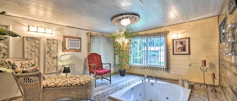 A spacious bathroom with a large bathtub, wicker furniture, and a potted plant.