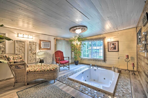 A spacious bathroom with a large bathtub, wicker furniture, and a potted plant.