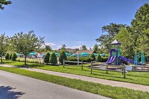 A playground with a slide and climbing structures, surrounded by a fence and trees.