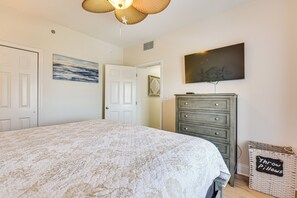 Een slaapkamer met een groot bed, een dressoir, een televisie en een mand met sierkussens.