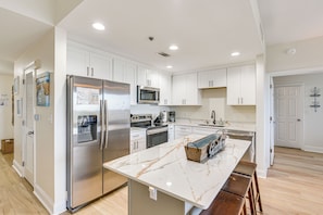 A modern kitchen with white cabinets, stainless steel appliances, and a marble countertop.