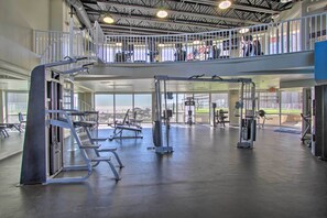 Een meerlaagse sportschool met diverse fitnessapparaten, een entresol met een leuning en grote ramen voor natuurlijk licht.