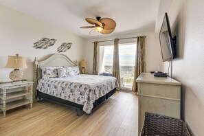 A bedroom with a bed, a nightstand, a dresser, a ceiling fan, and a TV mounted on the wall.