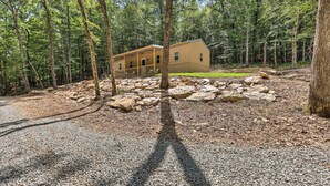 A cabin in a forest with a gravel driveway and large rocks in front. - Tallassee Cabin w/ Forest Views Near Creek! (Tallassee)