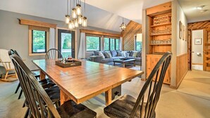 A spacious dining area with a wooden table and chairs, a built-in bookshelf, and large windows offering a view of the outdoors. - Family-friendly Stratton Gem Close to Slopes! (Stratton)