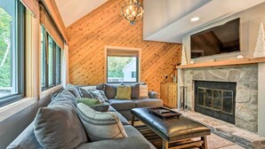 A modern living room with a stone fireplace, a large TV mounted above it, and a wooden ceiling. - Family-friendly Stratton Gem Close to Slopes! (Stratton)