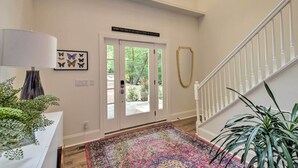 A hallway with a patterned rug, a white wall with butterfly art, a door with a sign, and a staircase with a white railing.