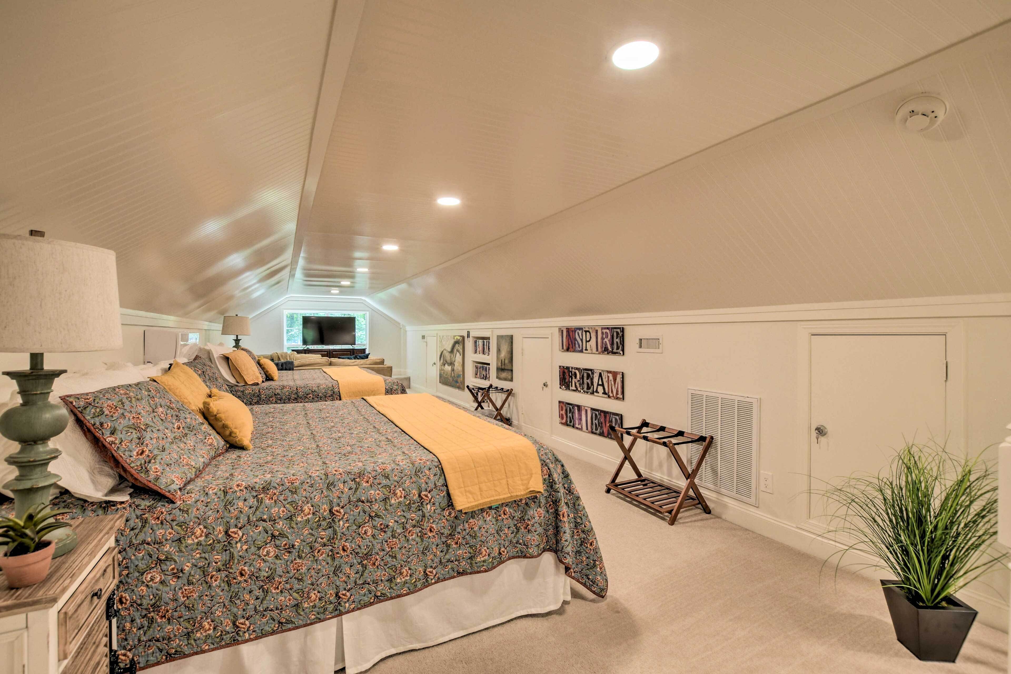 Ein geräumiges Schlafzimmer im Dachgeschoss mit zwei großen Betten, einem Fernseher und einem Deckenventilator.