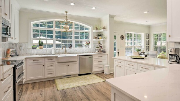 A spacious kitchen with white cabinetry, a large window, and a built-in oven.