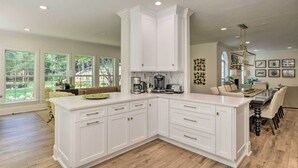 A spacious kitchen with white cabinetry, a large island, and a dining area with a chandelier.