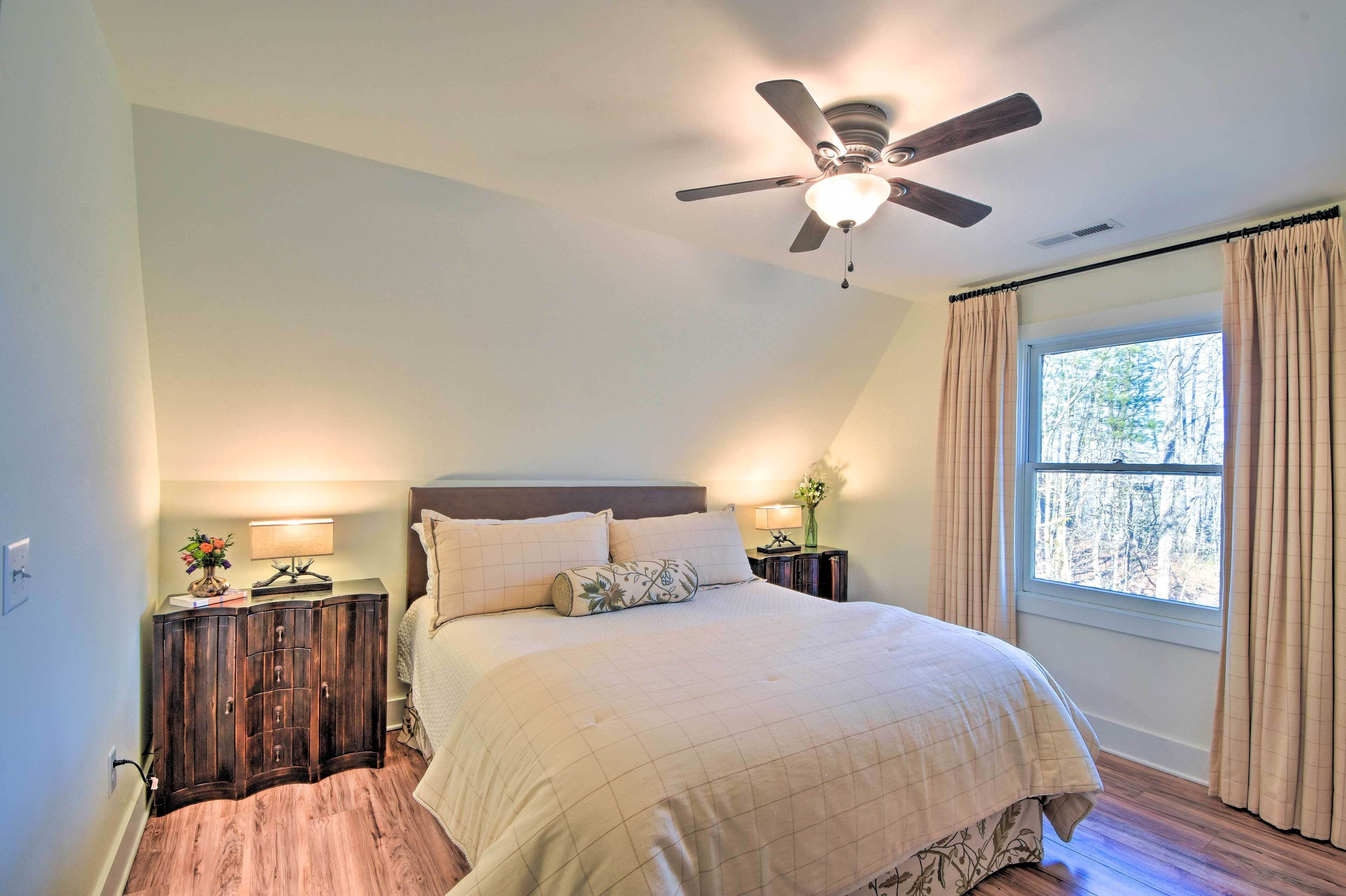 A bedroom with a bed, a ceiling fan, a nightstand with a lamp, and a window with curtains.