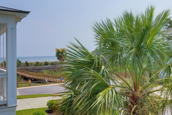 A coastal view with a palm tree, a wooden bridge, and a clear sky.