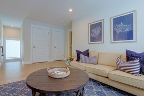 Ein Wohnzimmer mit rundem Holztisch, beiger Couch und zwei gerahmten Pflanzenbildern an der Wand.