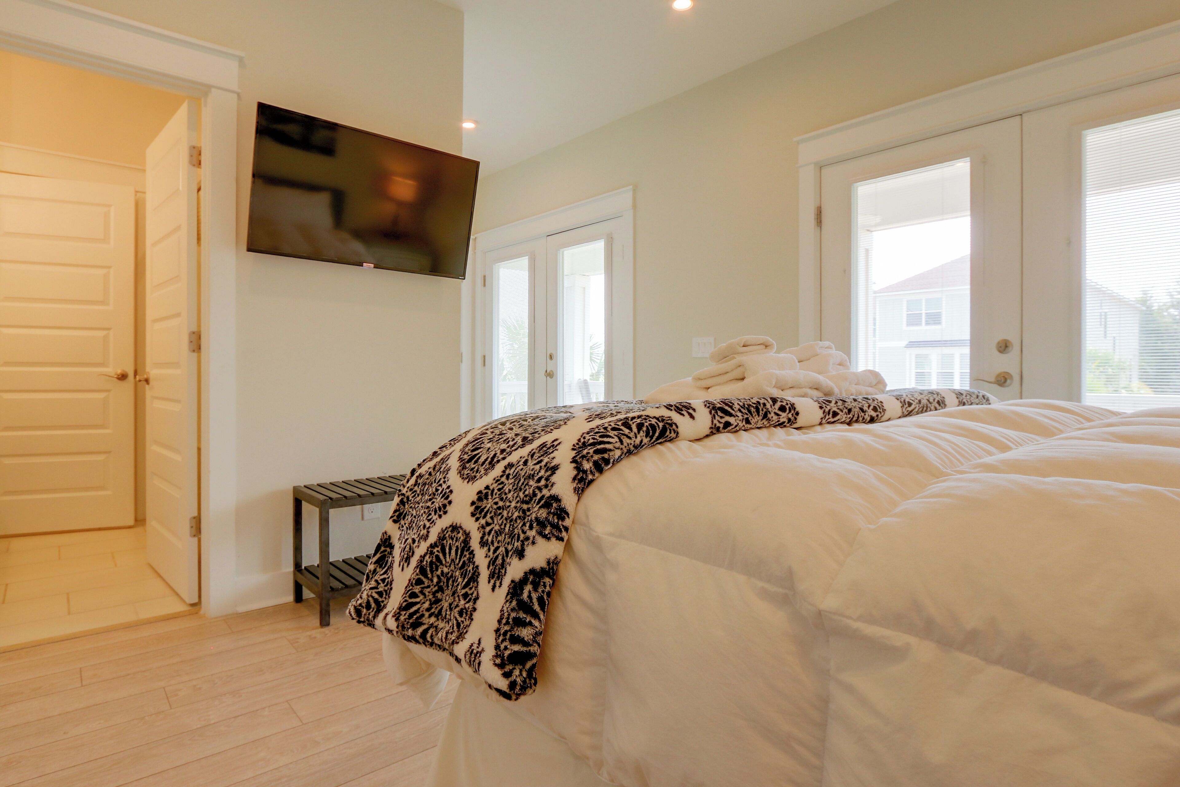 Un dormitorio con una cama grande, un televisor montado en la pared y una puerta que da a otra habitación.