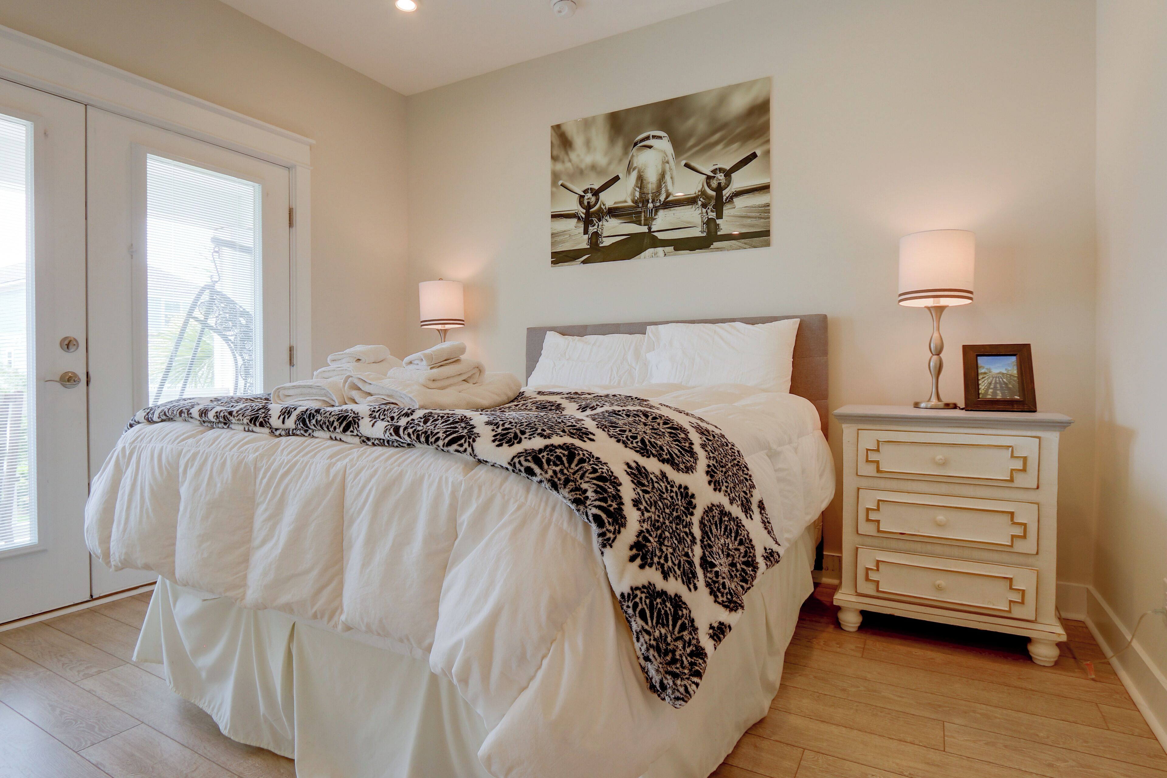 A bedroom with a bed, a nightstand, a lamp, a framed picture, and a door with blinds.