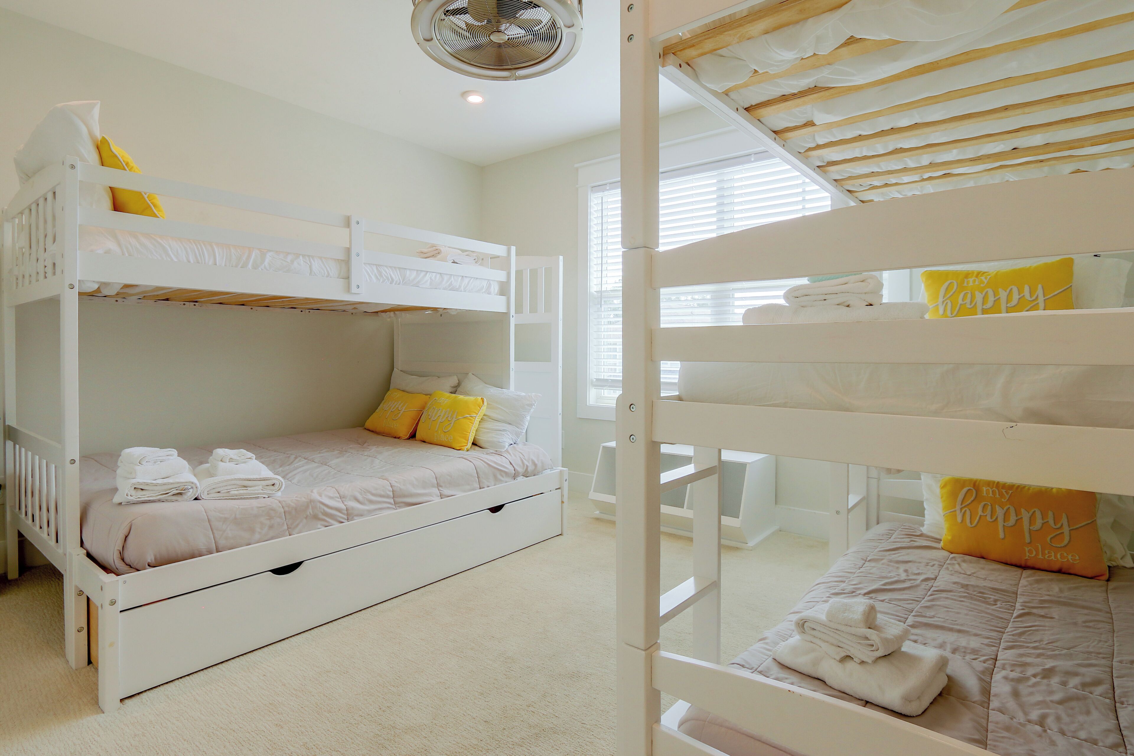 A bunk bed room with a ceiling fan, a window with blinds, and a 'my happy place' pillow.