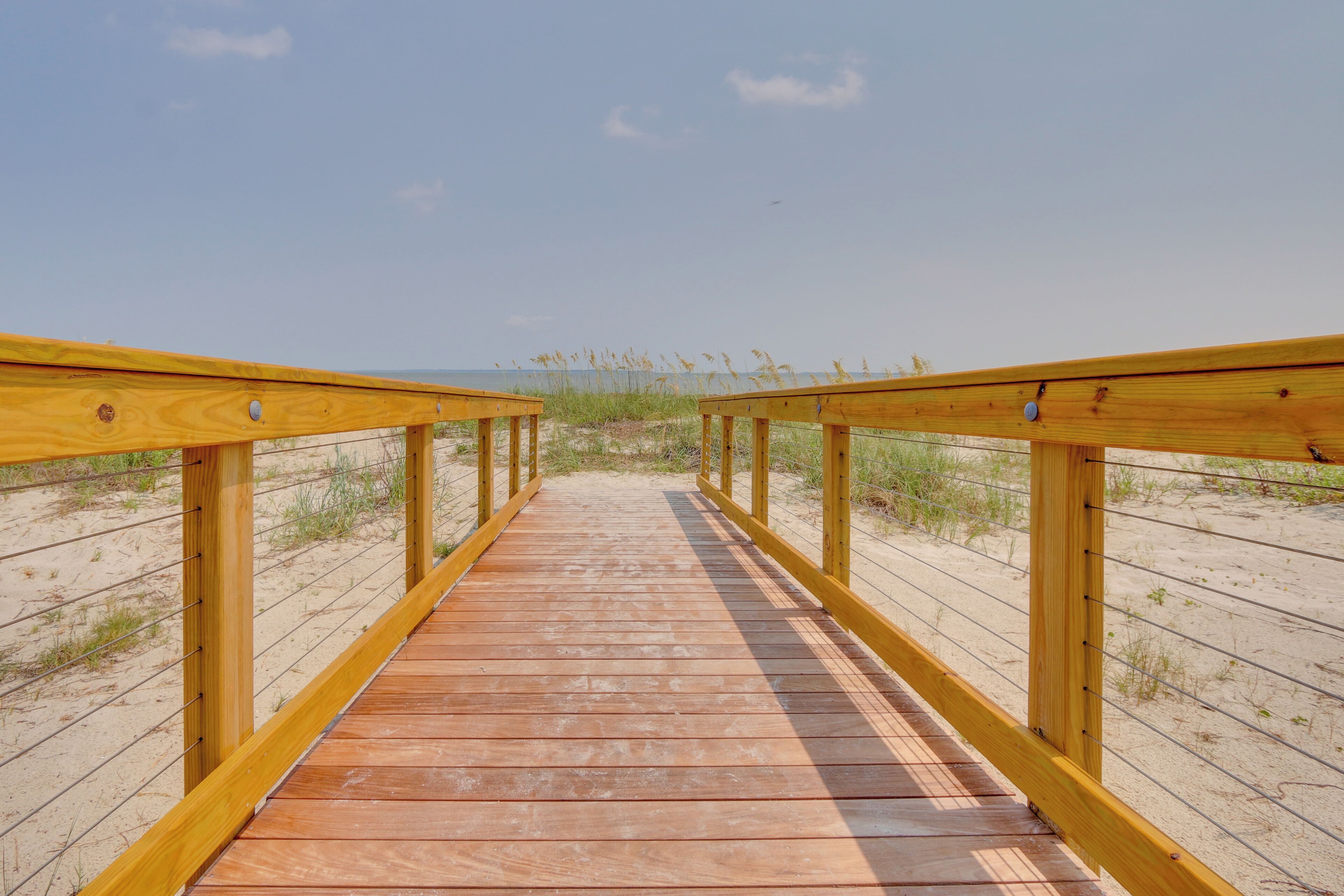 A wooden boardwalk leading to a beach with a clear sky.