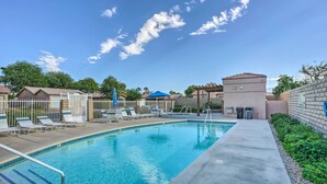 A swimming pool with lounge chairs and umbrellas, surrounded by a fence and buildings. - Indio Home w/ Resort Amenities, Near Festivals! (Indio)