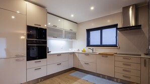 Una cocina moderna con armarios blancos, horno empotrado, ventana sobre el fregadero y campana extractora de acero inoxidable.