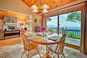 A cozy dining area with a wooden table and chairs, a stone fireplace, and a large window with a view of the mountains. - Smoky Mountain Vacation Rental Near Bryson City! (Bryson City)