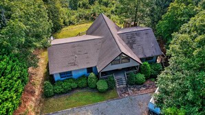 A house with a steeply pitched roof, surrounded by dense greenery and a small front yard.