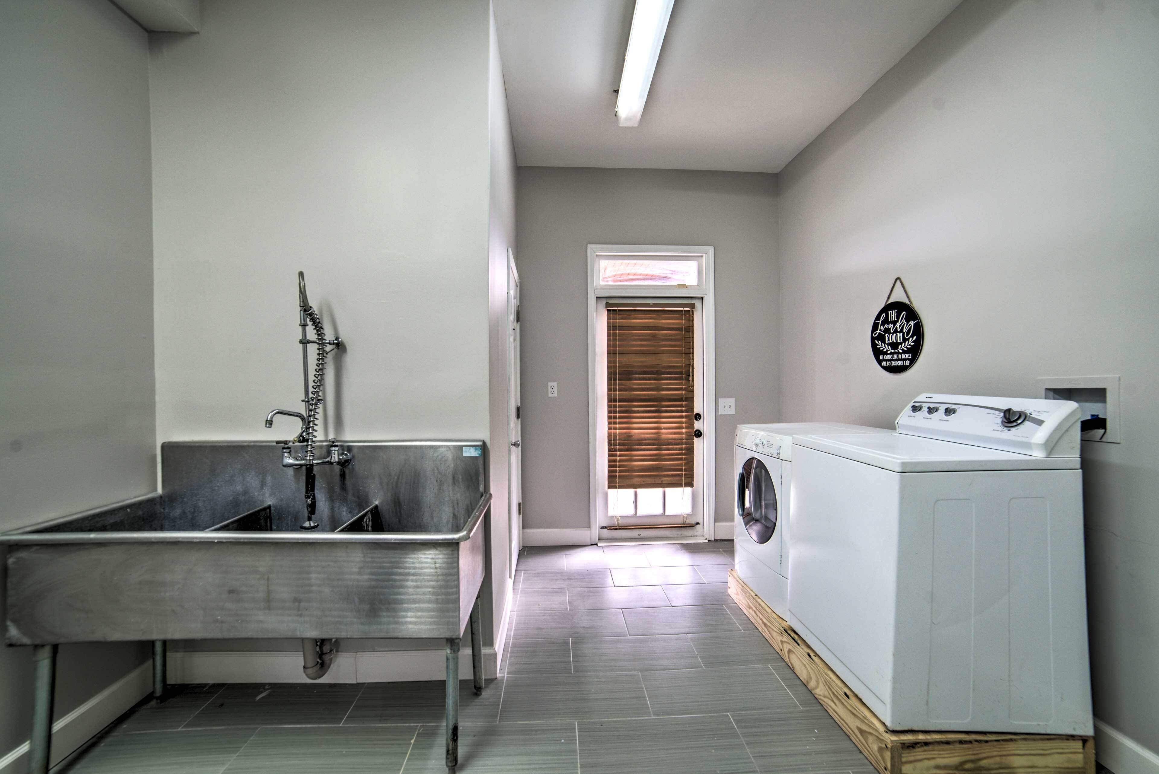 A laundry room with a stainless steel sink, a washing machine, and a door with blinds.