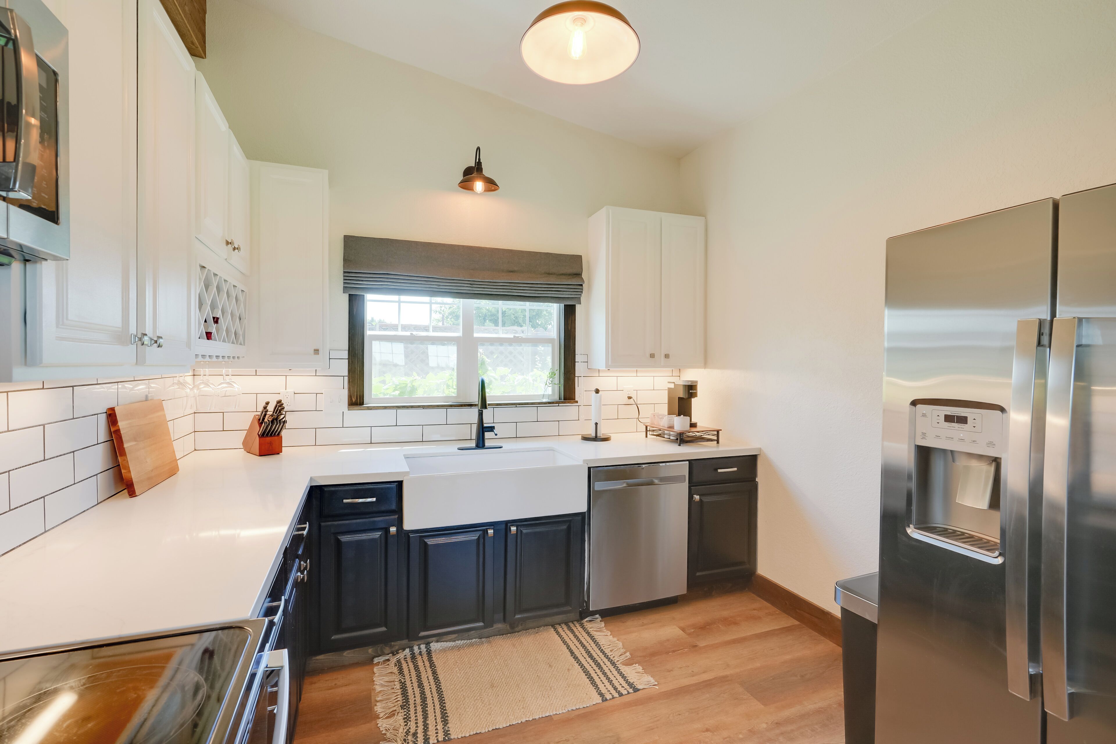 A modern kitchen with white cabinets, stainless steel appliances, and a large window.