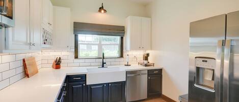 A modern kitchen with white cabinets, stainless steel appliances, and a large window.
