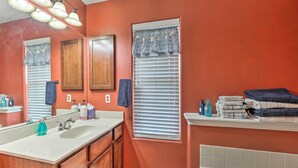 A bathroom with two sinks, wooden cabinets, a vanity, a window with blinds, and a shelf with towels. - Laguna Vista Home w/ Resort Perks Near Beach! (Port Isabel)