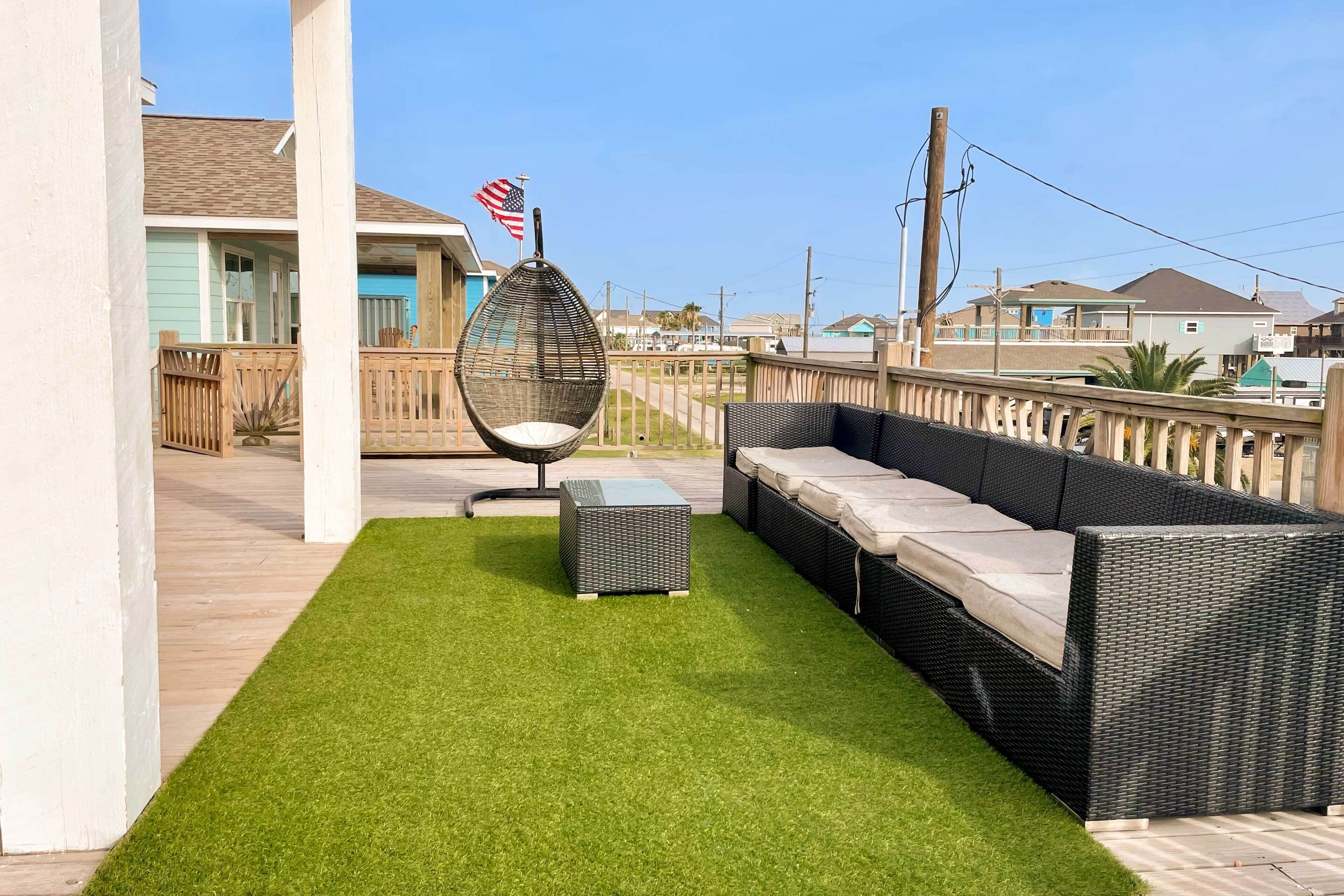 A patio with artificial grass, a wicker sofa, a hanging chair, and an American flag.