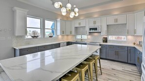 Una cocina moderna con encimeras de mármol blanco, armarios grises y detalles dorados.