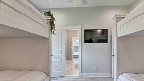 Un dormitorio con literas, ventilador de techo y vista a otra habitación.